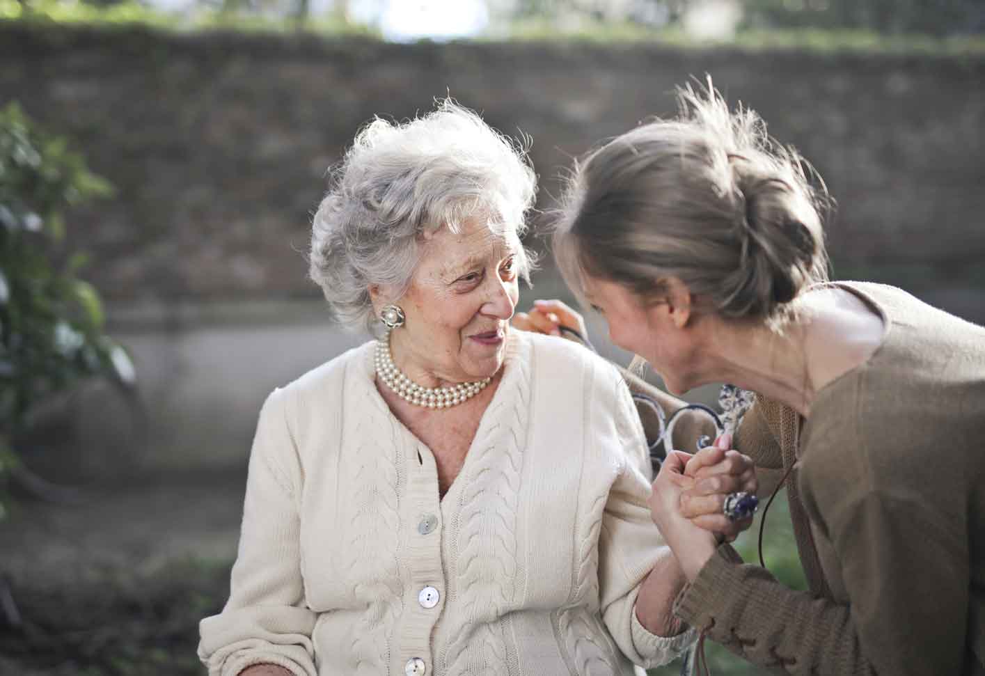 elderly lady sitting holding hands with mature daughter, smiling and looking into each others eyes